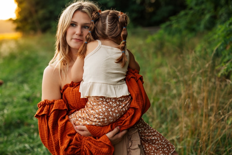 A mother holds her young daughter in her arms as she embraces her mother, they are outside in the grass