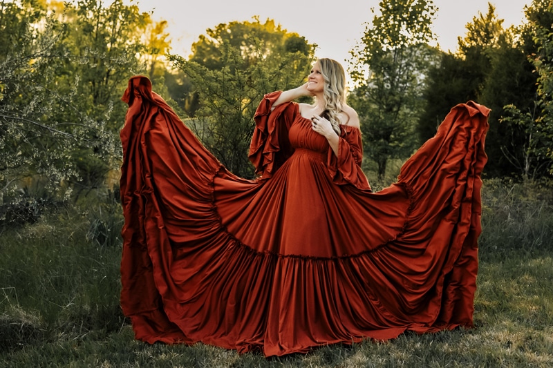 A woman stands among trees in a red dress spread out